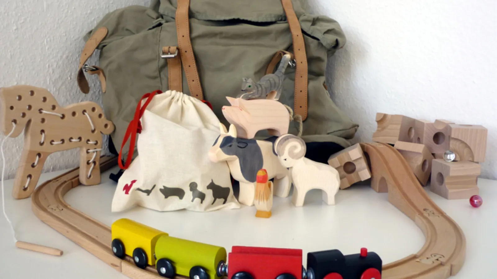 Schienen und Zug einer Spielzeugeisenbahn aus Holz,dazwischen liegt ein Kinderrucksack als mobiles Kinderzimmer der FH Potsdam