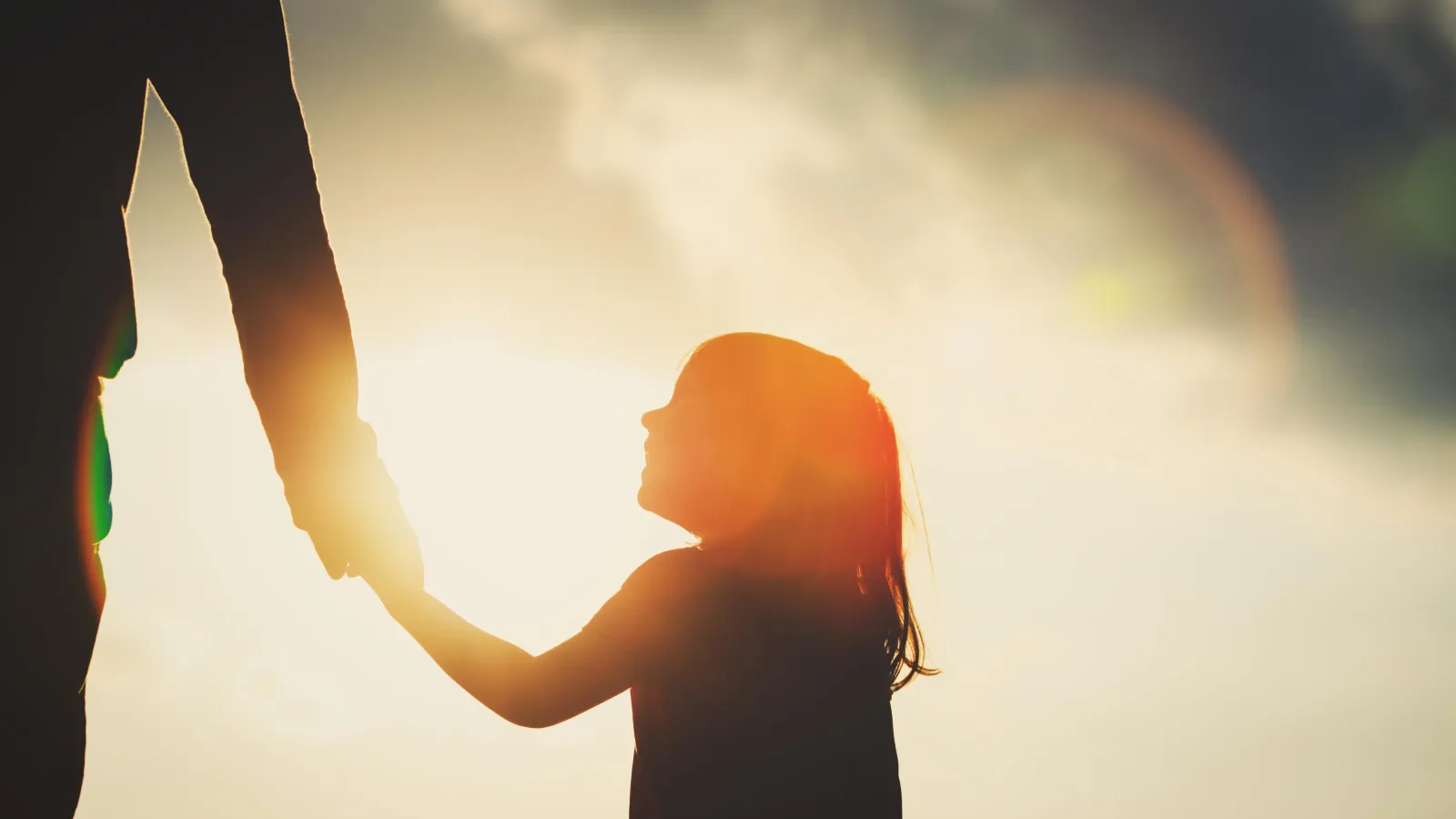 Silhouette eines Kindes, das an der Hand eines Erwachsenen l?uft, im Hintergrund die Sonne