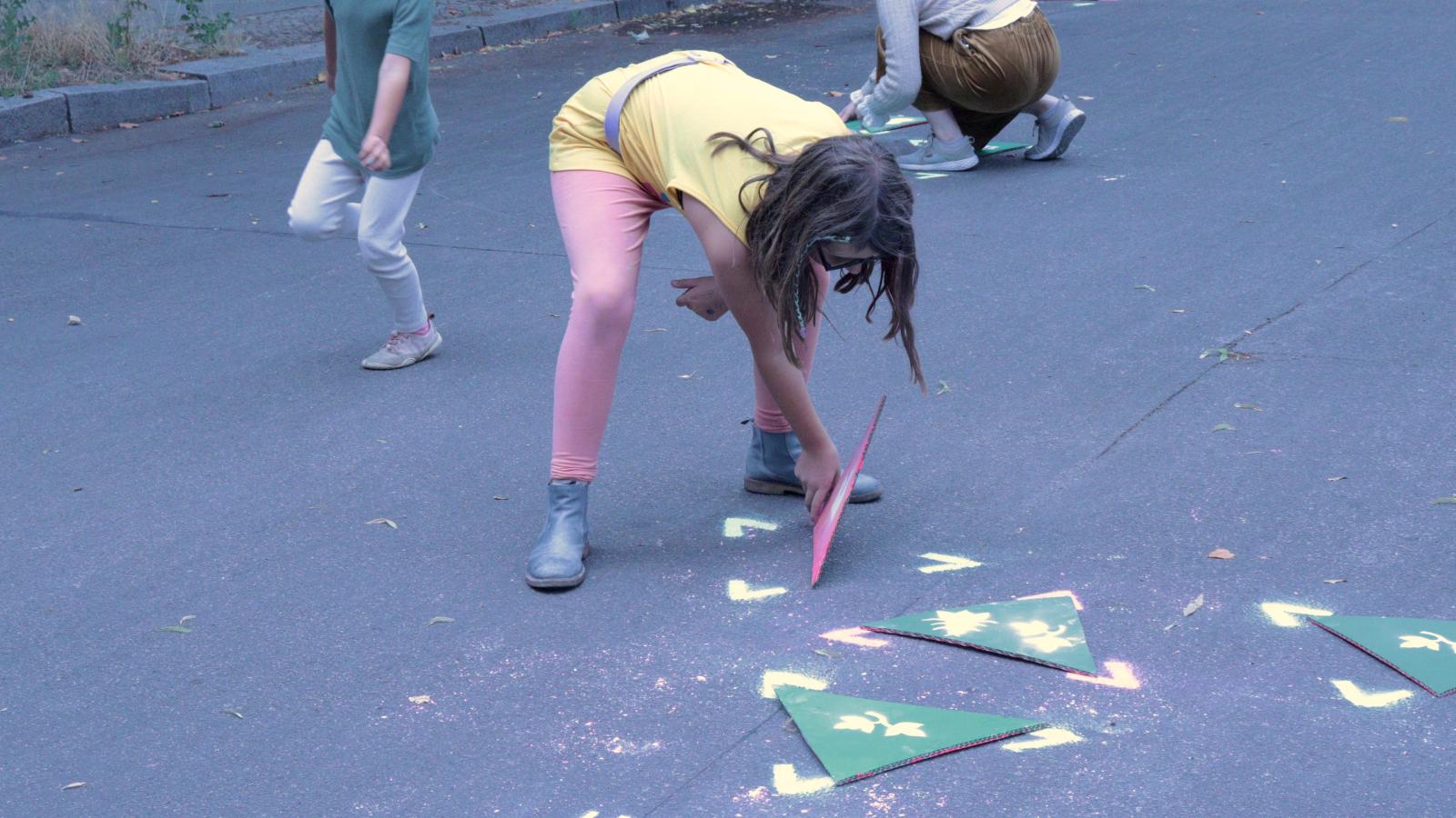 Kinder spielen mit grnen Dreiecken aus Pappe auf dem Asphaltboden