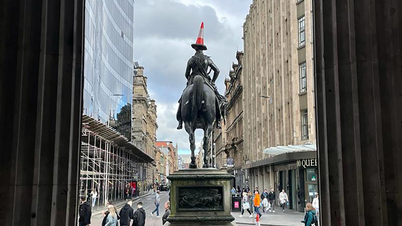 Der Blick fhrt aus dem Eingang des Gallery of Modern Art Glasgow heraus auf eine Statue auf einem Pferd die man von hinten sieht. Auf dem Kopf der Figur ist ein Verkehrskegel balanciert.
