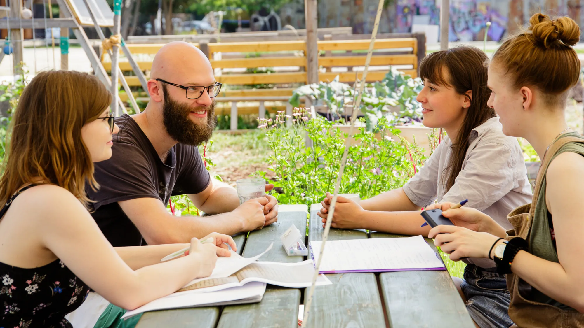 Studierende sitzen zusammen an einem Tisch im Campusgarten der FH Potsdam