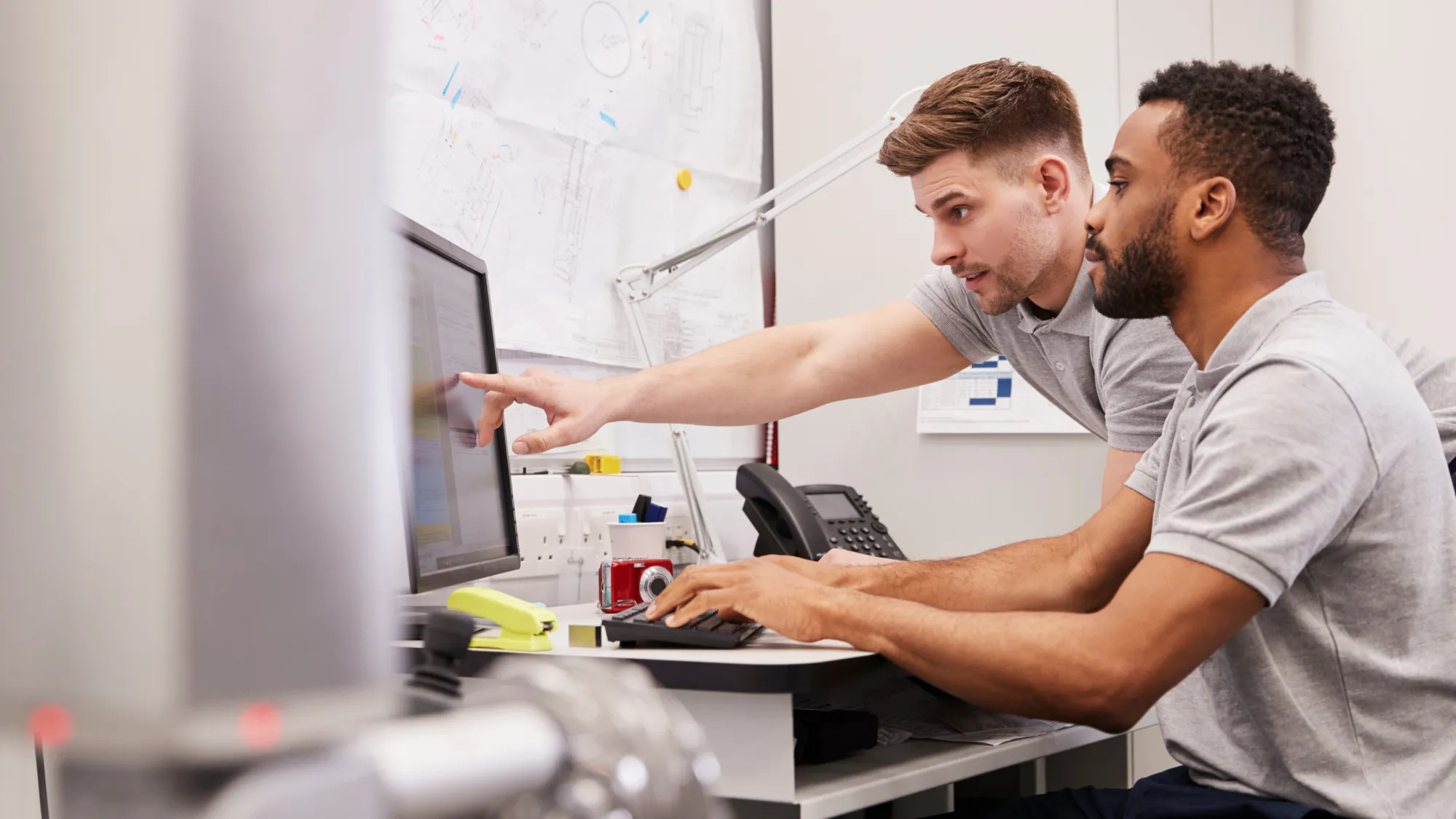 Zwei Personen schauen auf einen PC-Monitor, einer zeigt mit einem Finger darauf