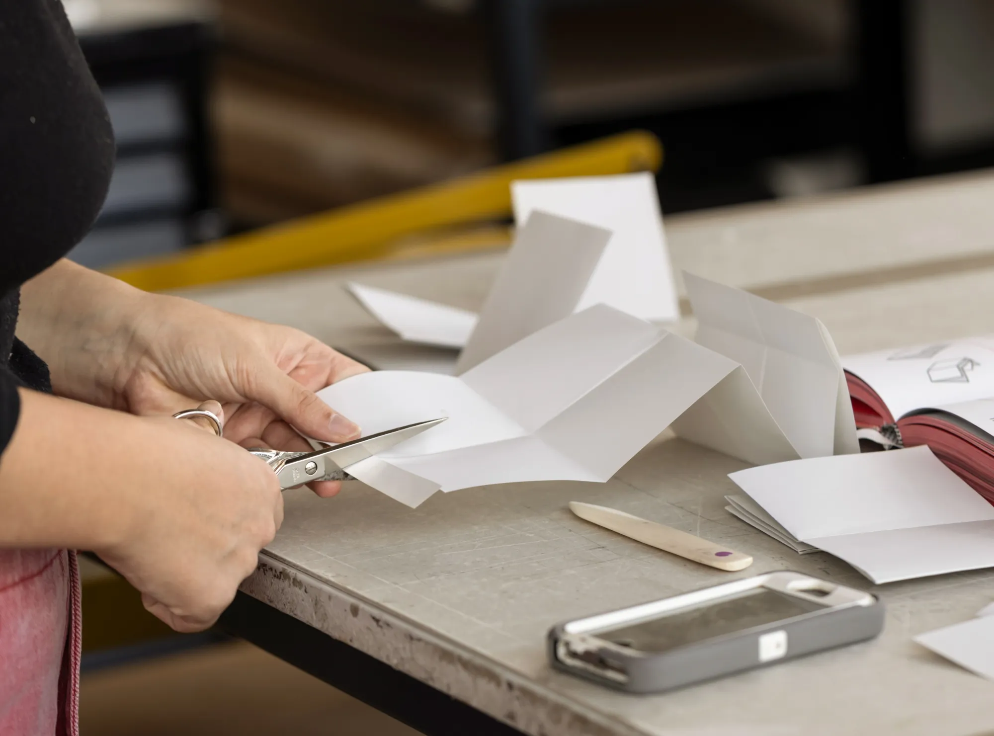 Eine Person schneidet an einem Arbeitstisch ein Papier zu.