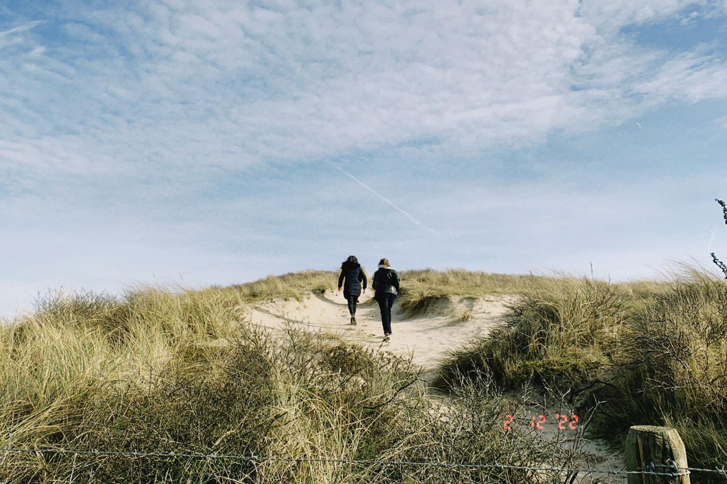 Zwei Personen laufen auf einem Sandweg eine Dne Hoch. Der blaue Himmeln ist leicht bew?lkt. 