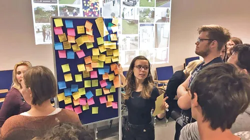 Studierende halten eine Pr?sentation vor einer Wand mit bunten Zetteln